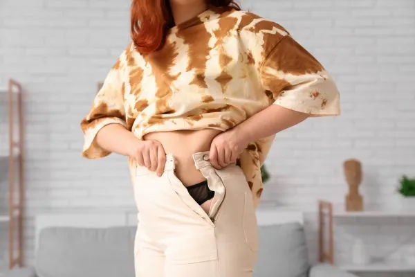 Image of woman trying to do her trousers up after pregnancy weight gain Tetbury